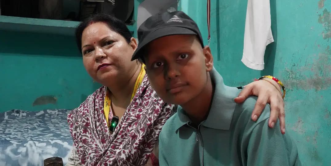 Woman stands with arm around a young person against a teal wall