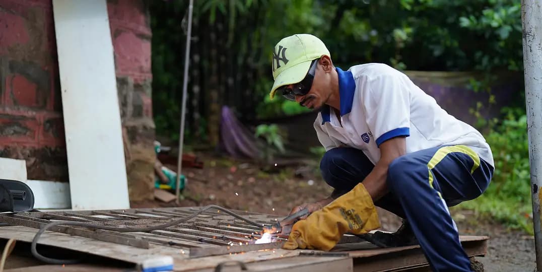 Man welds metal outdoors, sparks flying from his work