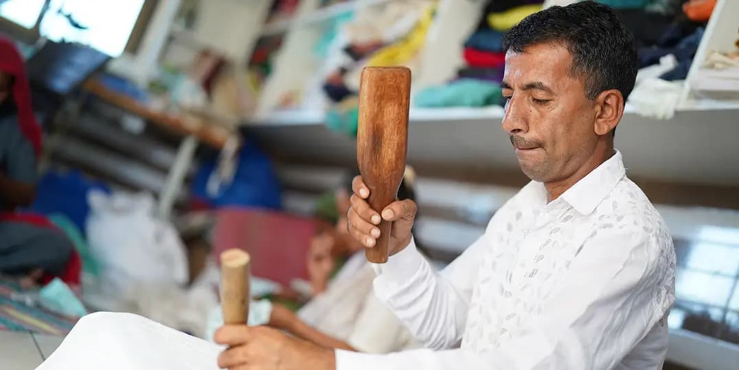 Craftsman carves wood by hand amid stacks of fabric