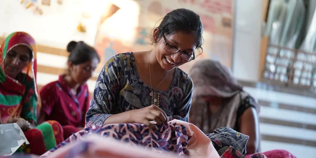 Smiling woman embroiders fabric alongside other women in a circle